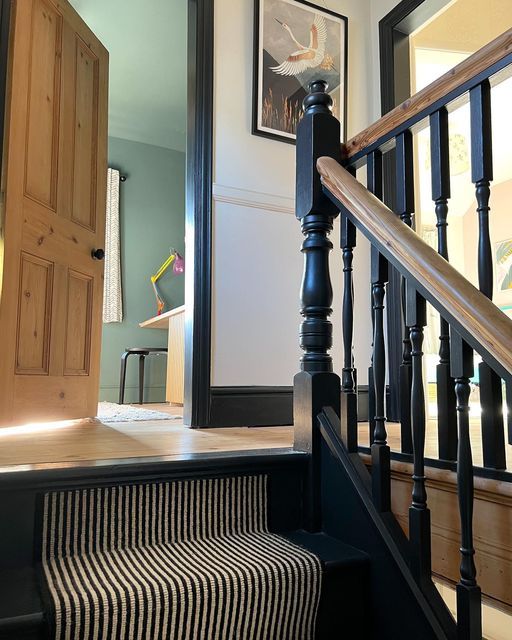 a staircase with black and white striped carpet next to a wooden bannister door