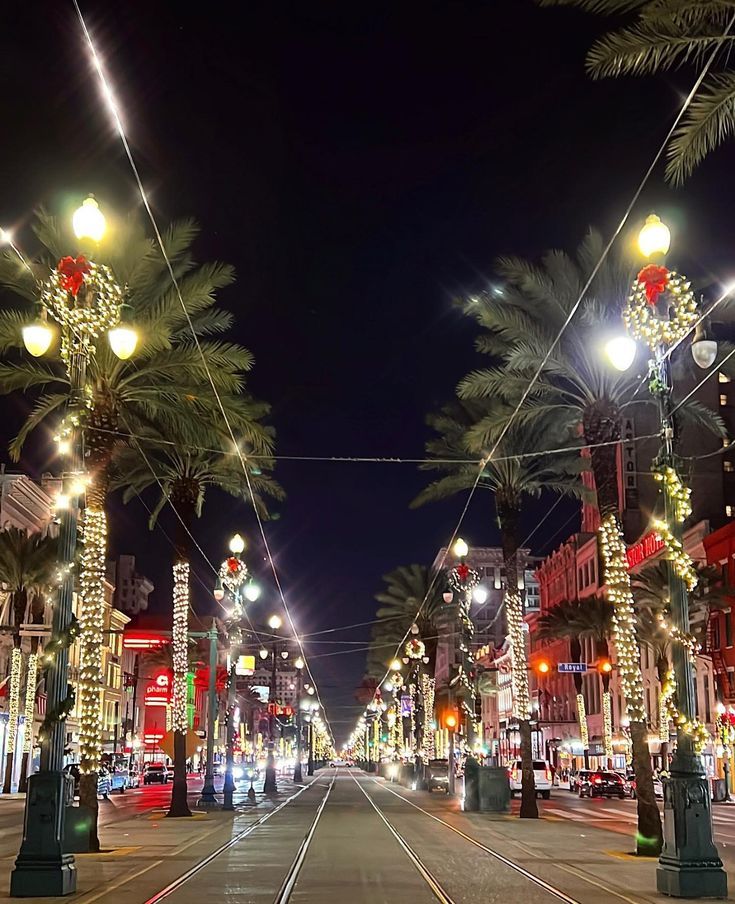 an empty city street at night with palm trees on both sides and lights all around