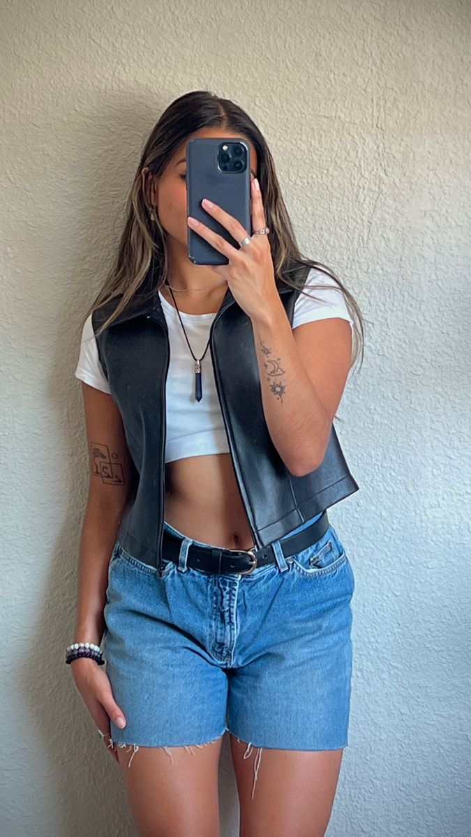 Mirror picture of girl wearing plain white crop top with black leather vest over, jean shorts with black belt, and crystal necklace Festival Vest Outfit, Vest With Tank Top Outfit, Cropped Leather Vest Outfit, Cropped Jean Vest Outfit, Outfits For The Fair Summer, Am Concert Outfit, Leather Vest Outfit Aesthetic, Cropped Vest Outfit Street Styles, Black Leather Vest Outfits For Women