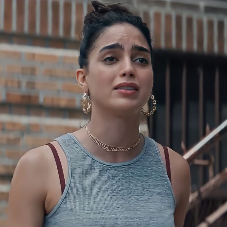 a woman in grey tank top standing next to stairs and brick building with large gold hoop earrings on her head