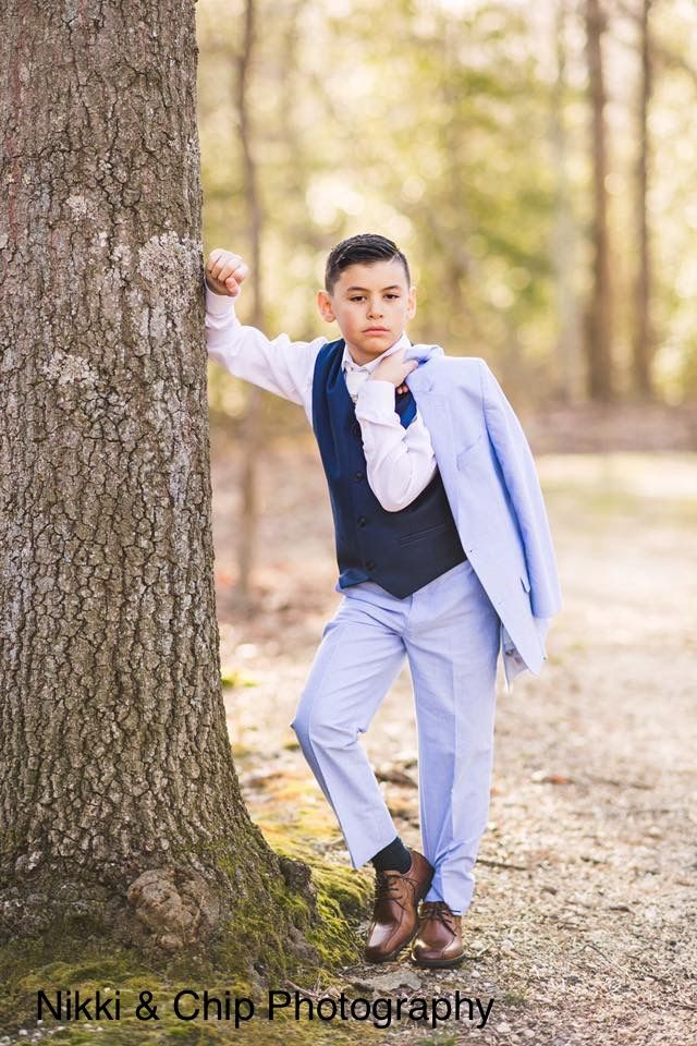 a young boy leaning against a tree in the woods wearing a blue suit and bow tie