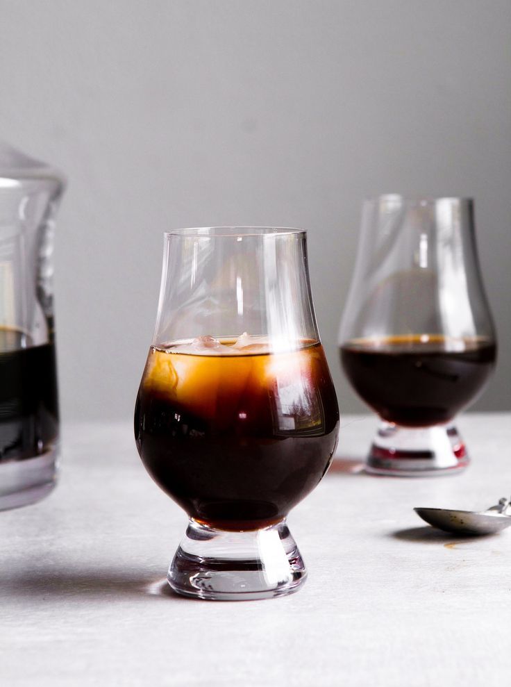 two glasses filled with liquid sitting on top of a table next to a spoon and glass container