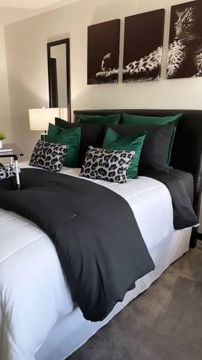 a bed with black and white sheets, green pillows and pictures on the wall above it