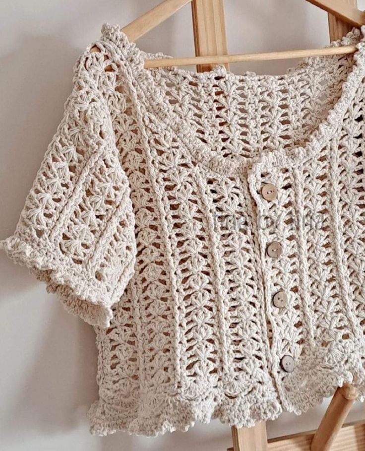 a crocheted sweater hanging on a wooden hanger