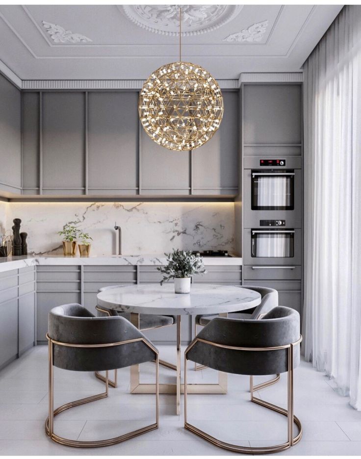 a kitchen with grey cabinets and white marble counter tops, an oval dining table surrounded by gray chairs