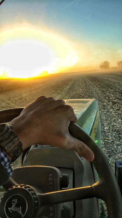 a man driving a tractor in the middle of a field at sunset, with his hand on the steering wheel