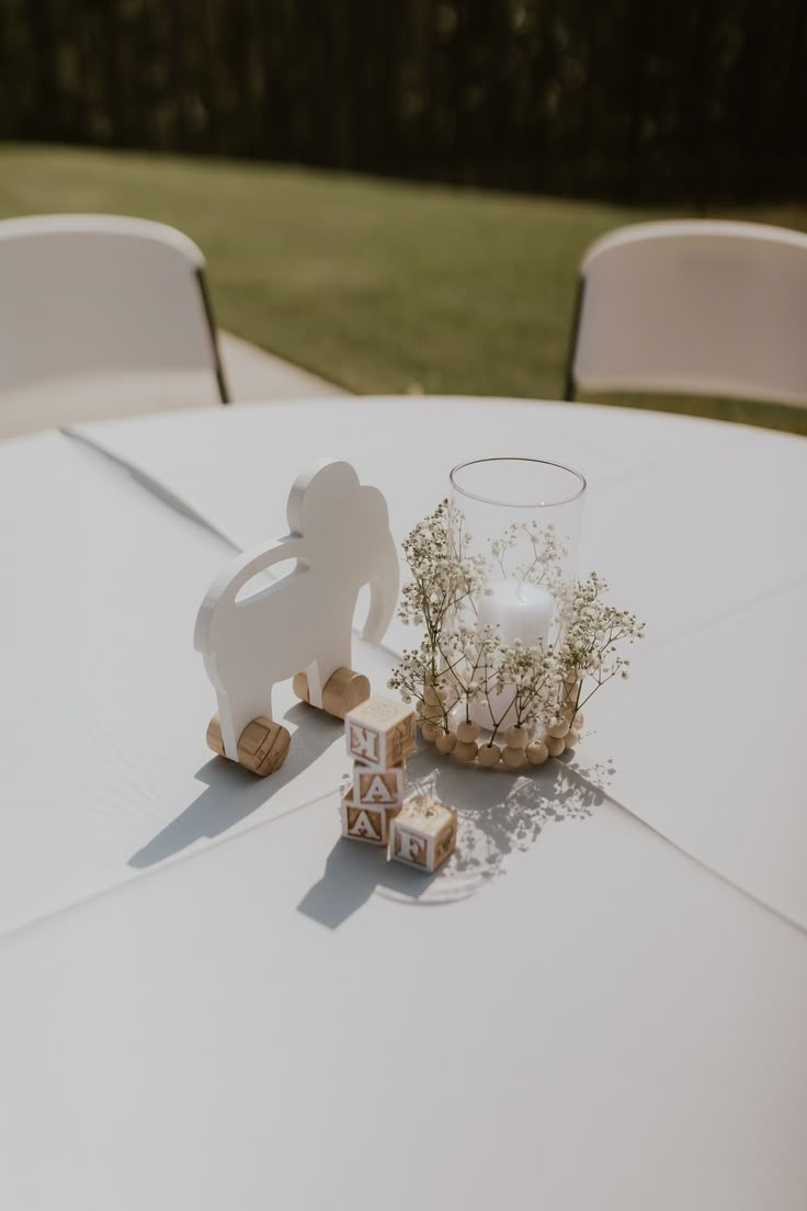 a white table topped with a vase filled with flowers next to small wooden animals on top of it