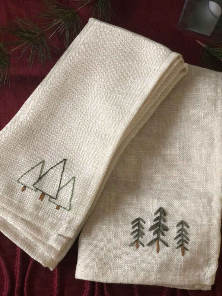 two white towels with embroidered trees on them sitting next to a christmas tree ornament