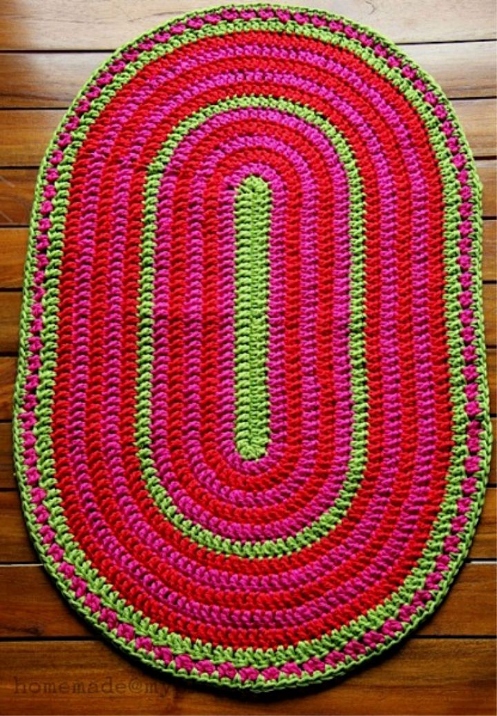 a crocheted rug is laying on a wooden floor with yarn and scissors next to it