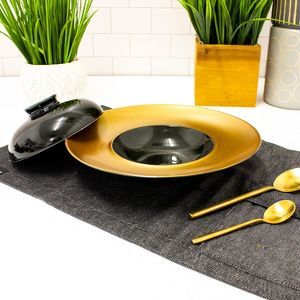 a black and gold place setting on a white table with green plants in the background