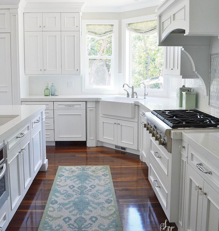 a large kitchen with white cabinets and wood flooring, along with an area rug