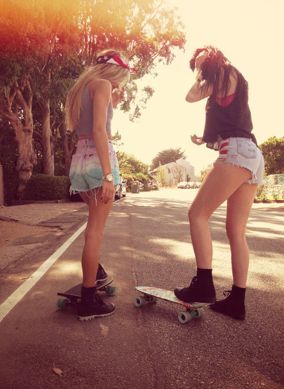 two girls standing on skateboards in the middle of the road talking to each other