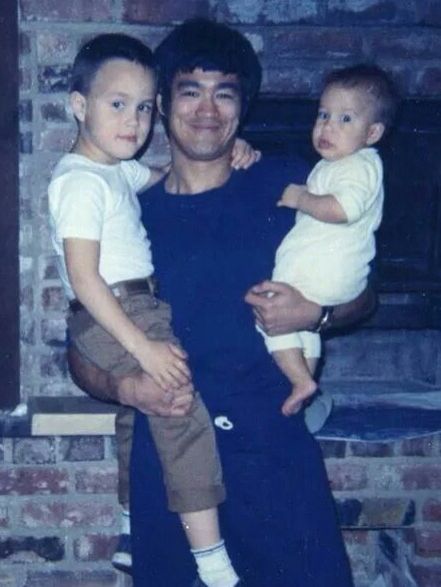 a man holding two small children in front of a fire place with a brick wall