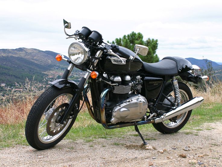 a black motorcycle parked on top of a dirt road next to a lush green hillside