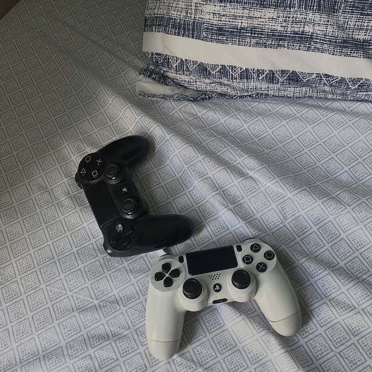 two video game controllers sitting on top of a bed next to each other in front of a pillow