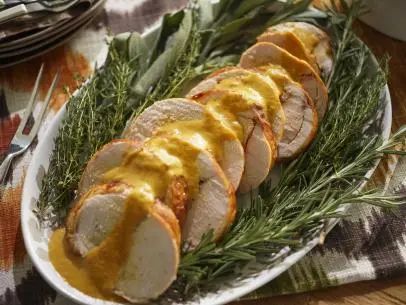 a white plate topped with sliced turkey covered in gravy and garnished with fresh herbs