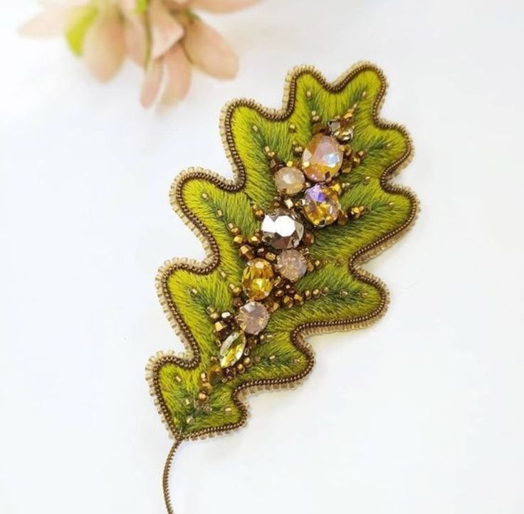 a brooch with green leaves and crystal stones on it's side, sitting next to a flower