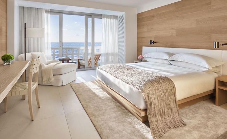 a bedroom with a bed, desk and chair next to a large window overlooking the ocean