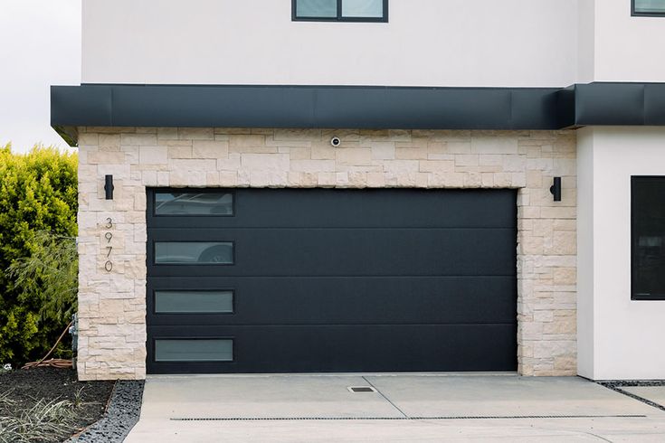 a black and white garage door in front of a brick building with bushes behind it