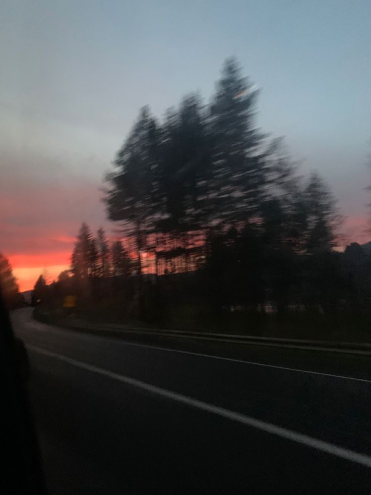 the sun is setting behind some trees on the side of the road as seen from inside a car