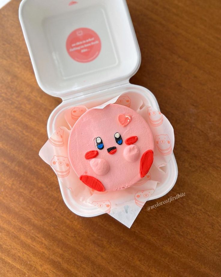 a pink cake in a plastic container on top of a wooden table next to a white plate