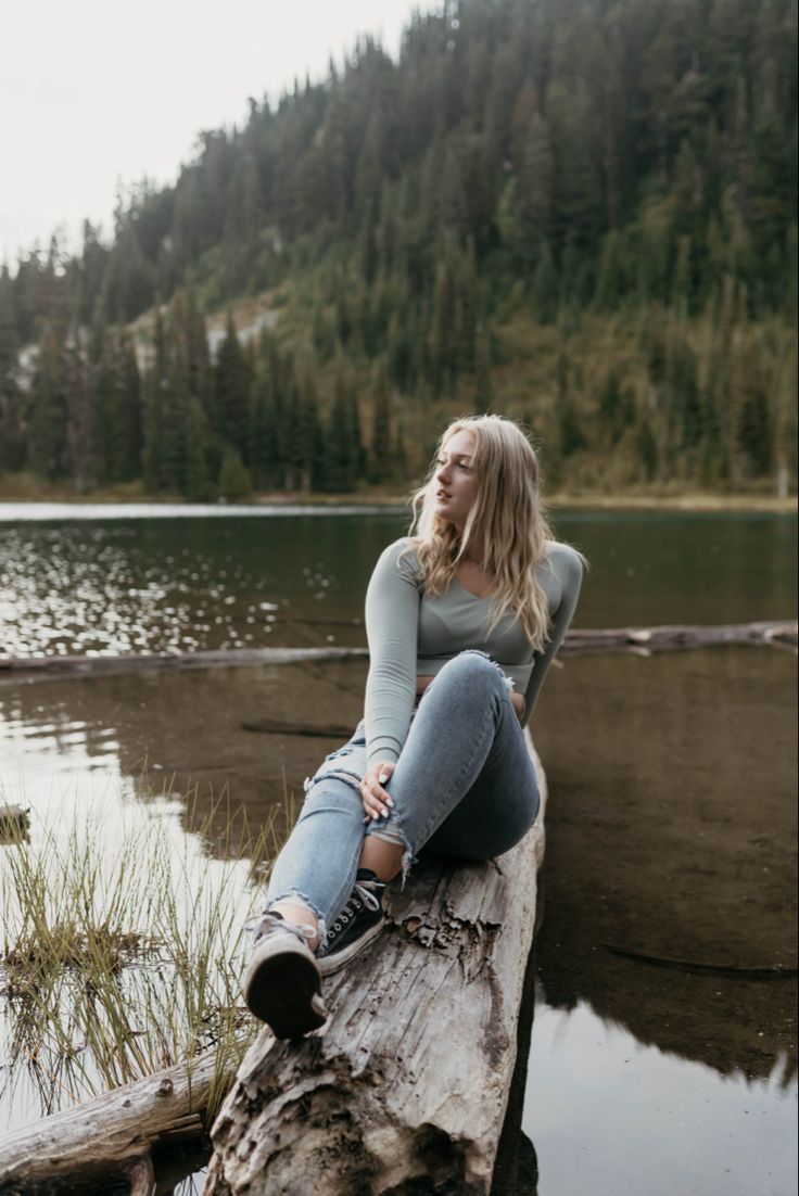 a woman sitting on top of a log next to a lake