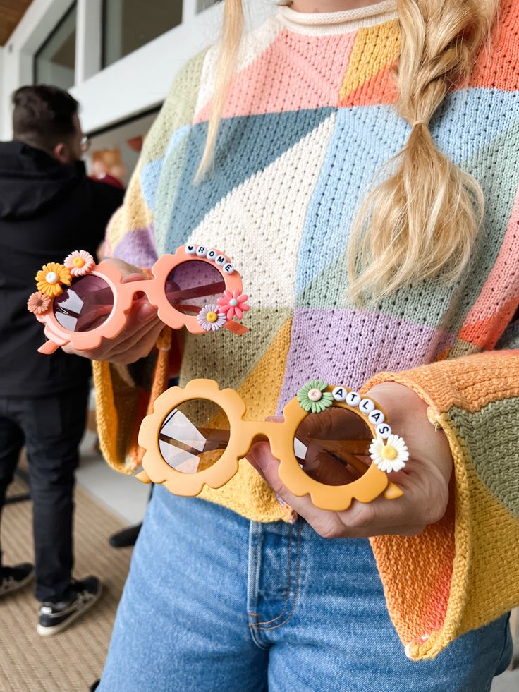 a woman wearing sunglasses with flowers on her fingers and holding them up to the camera