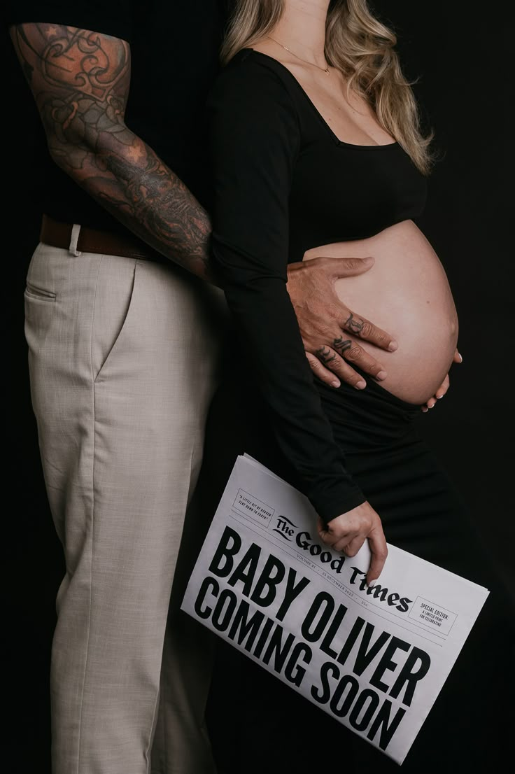 a pregnant woman holding a sign next to a man with tattoos on his arm and belly