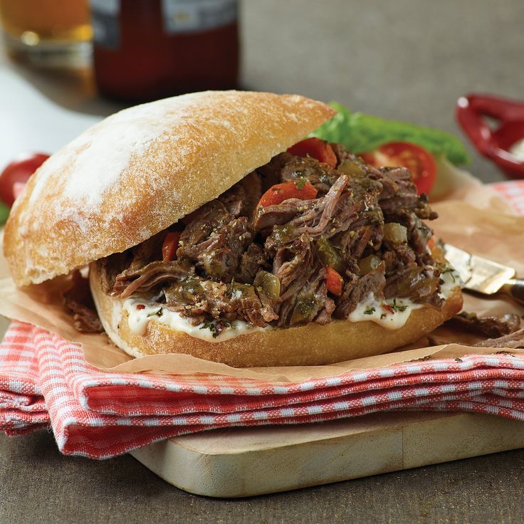 a pulled pork sandwich on a wooden cutting board with a red and white checkered napkin