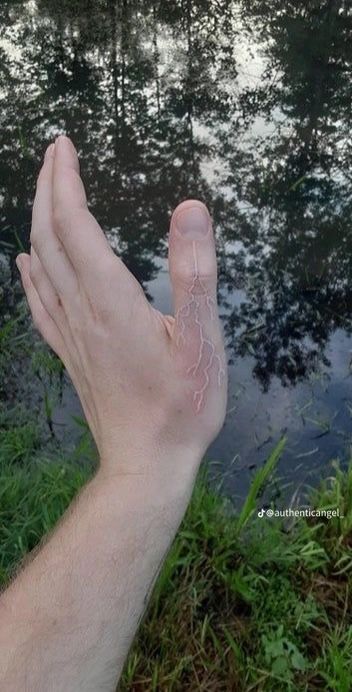 a person's hand holding something in front of a body of water with trees and grass