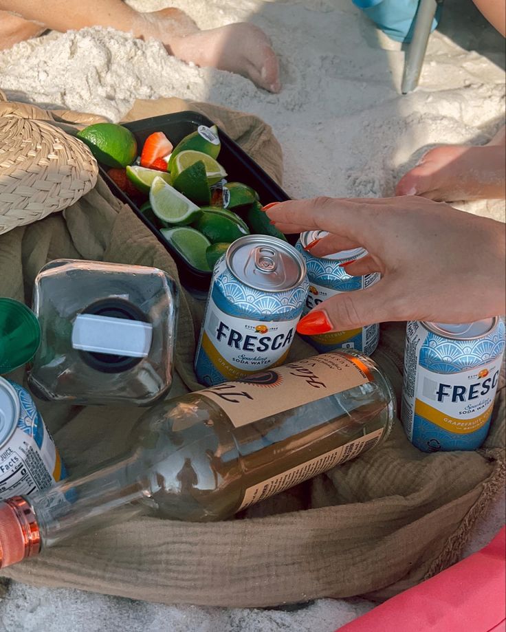 a person is sitting on the beach with several cans of sodas and drinks in front of them