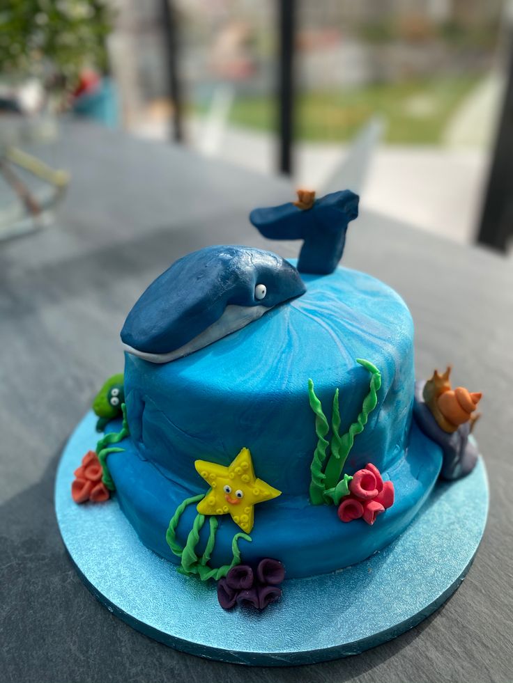 a blue cake with a whale on top and sea animals around the edges is sitting on a table