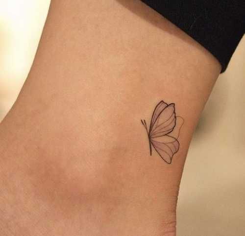 a small butterfly tattoo on the side of a woman's ankle, with black ink