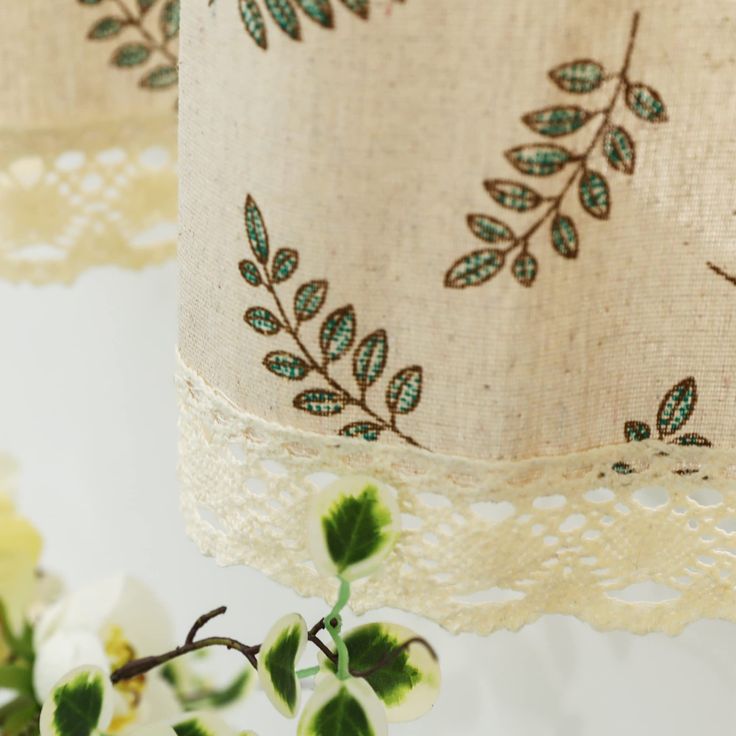 two lampshades with green leaves on them and lace trimming around the edges