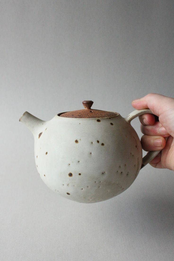 a hand holding a ceramic teapot with brown speckles