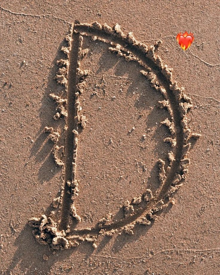 the letter d is drawn in the sand with a red heart on it's side