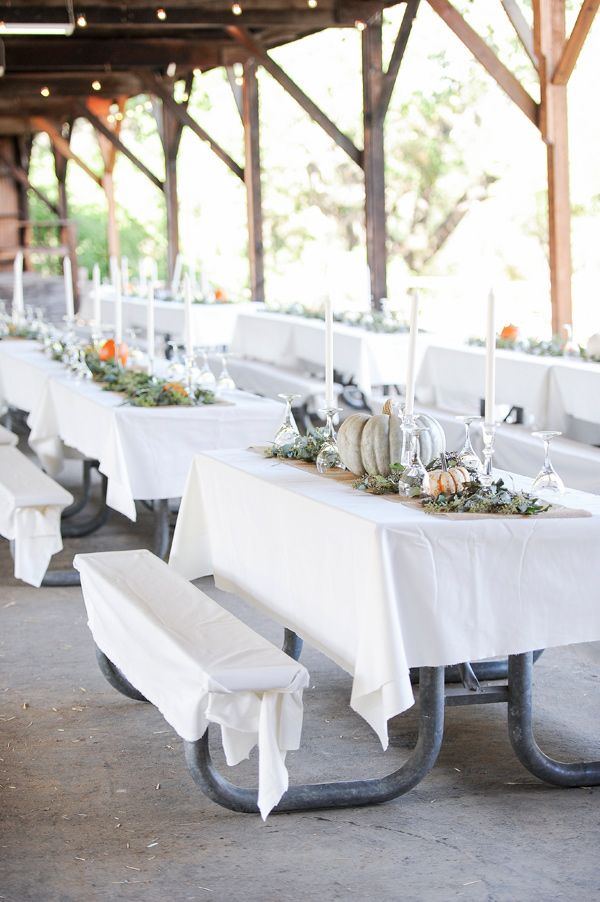 a long table with white linens and candles is set up for an outdoor event