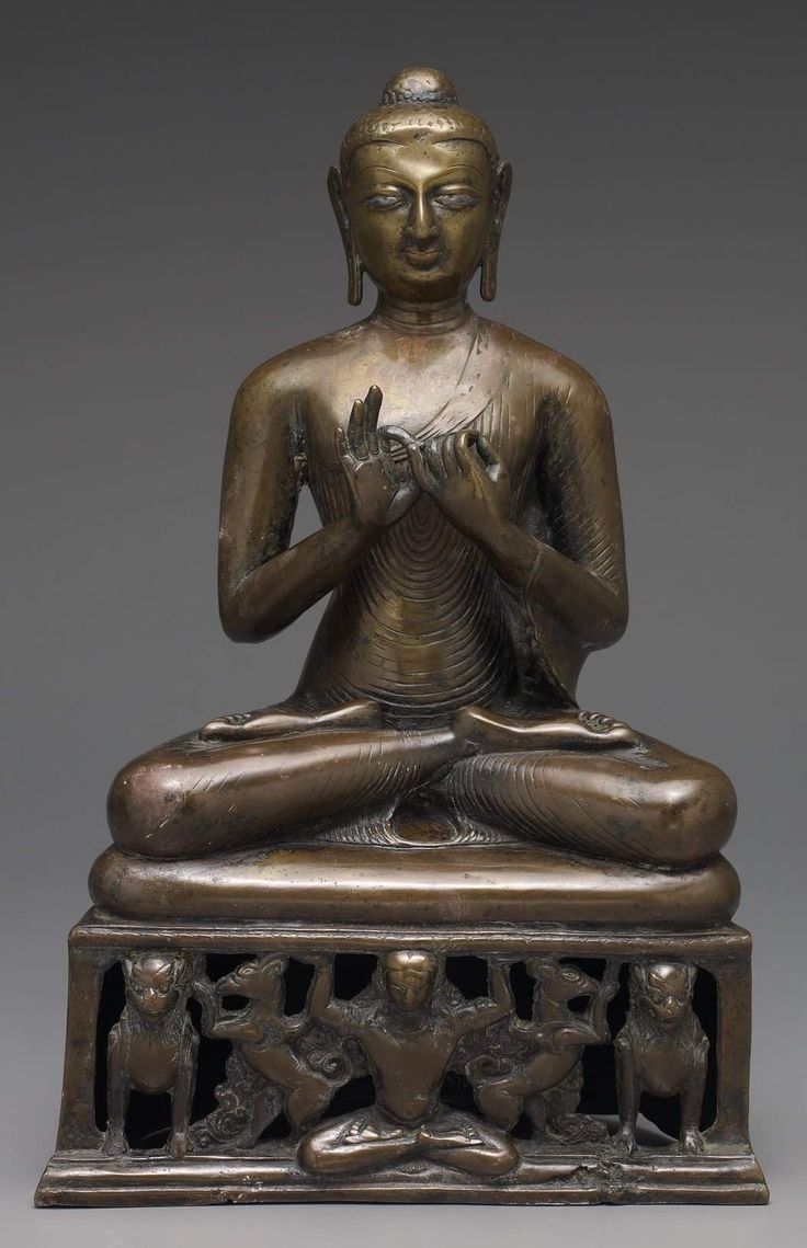 a bronze buddha statue sitting on top of a wooden stand with two hands in the air