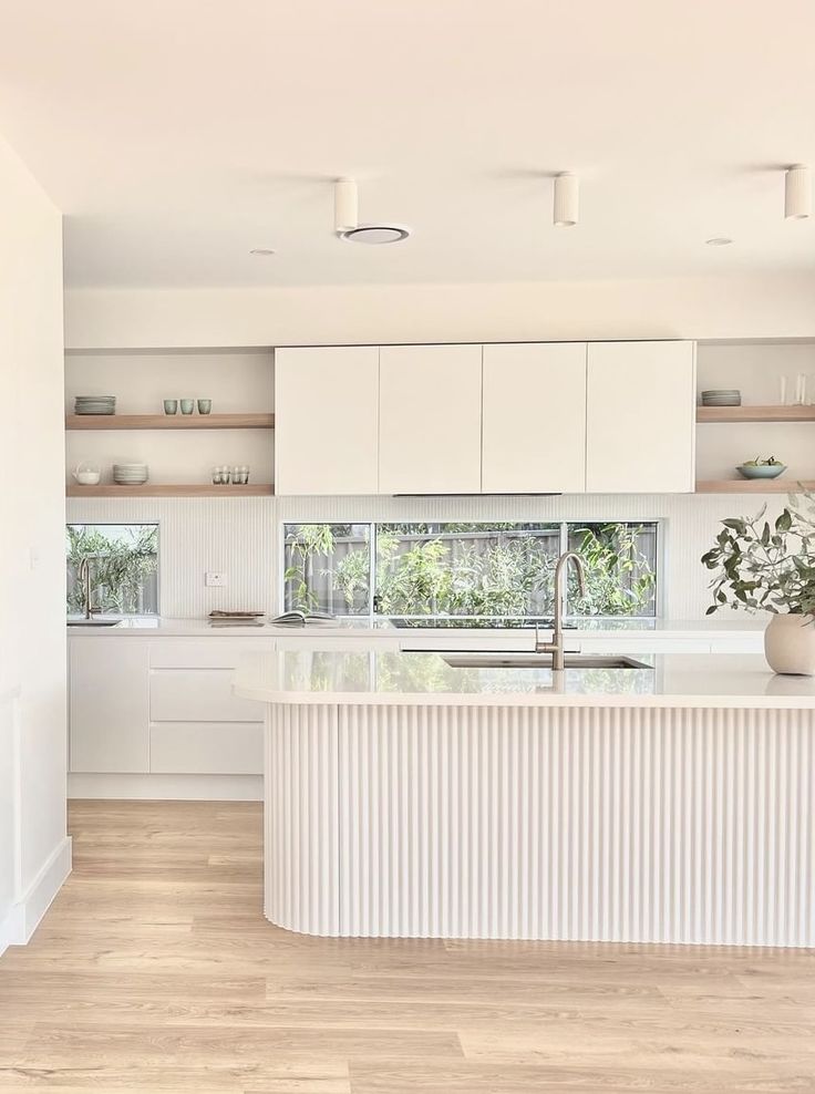 a large kitchen with white cabinets and wooden floors is pictured in this image, there are plants on the counter