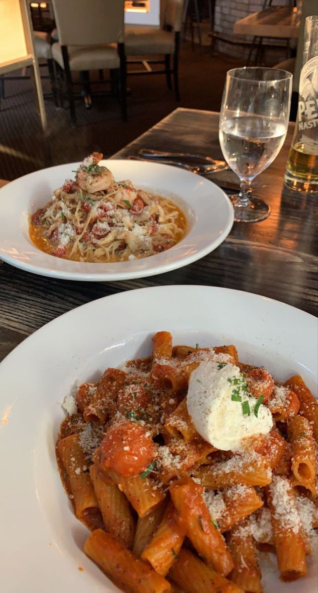 two plates of pasta with sauce and parmesan cheese on the side at a restaurant