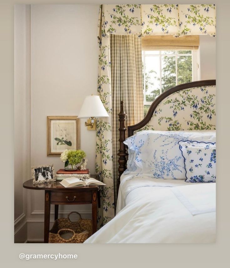 a bed with white sheets and blue flowers on the headboard in a bedroom next to a window