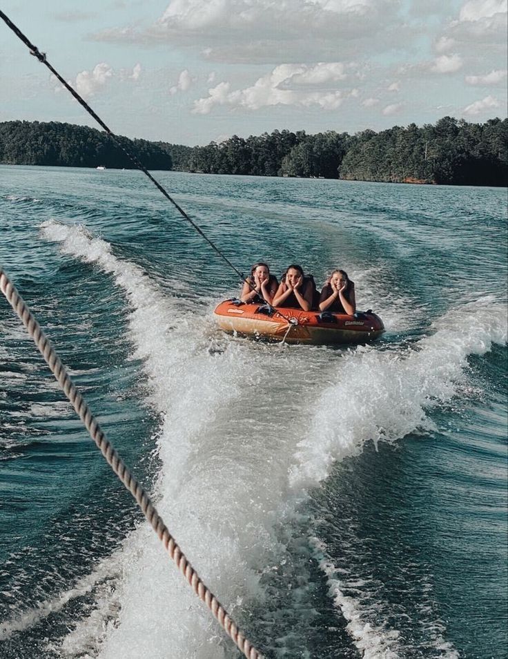 three people are riding in an orange boat on the water while being pulled by a rope