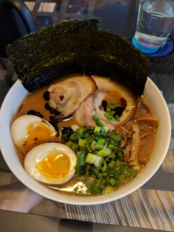 a bowl of ramen with an egg, meat and vegetables in it on a table