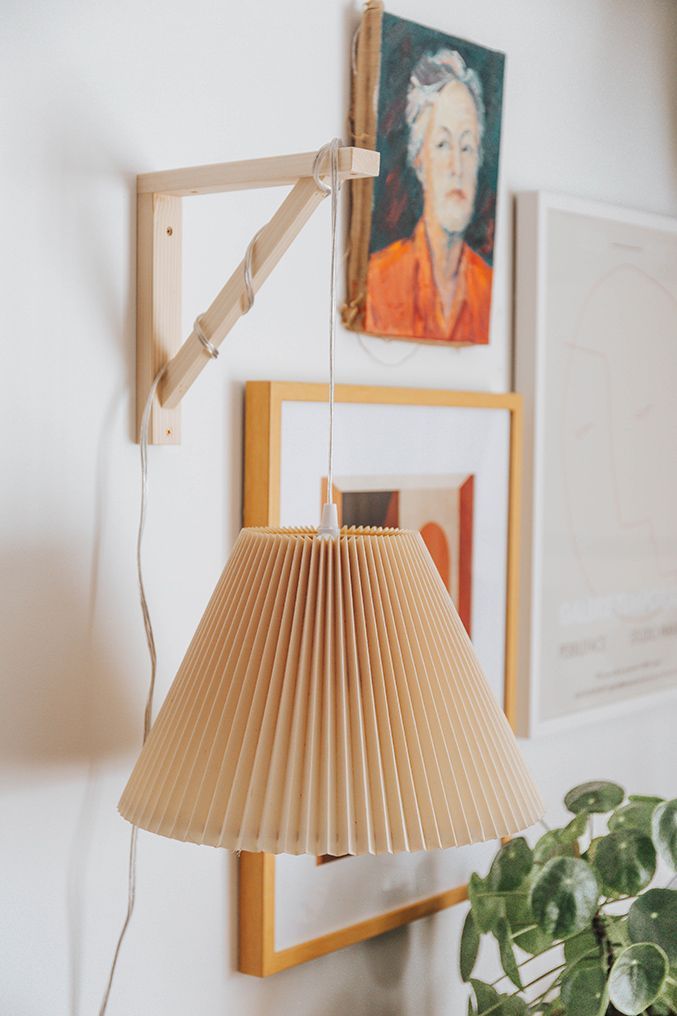 a lamp hanging from the side of a white wall next to a potted plant