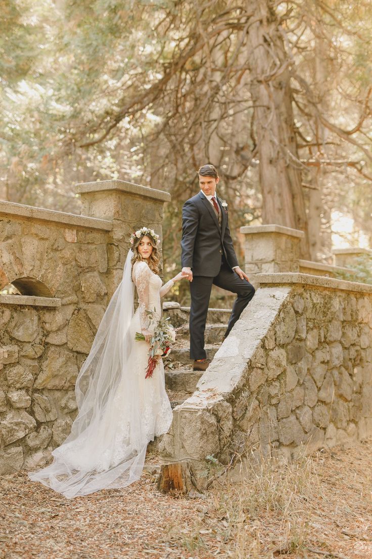 a bride and groom standing on the stone steps in front of trees at their wedding