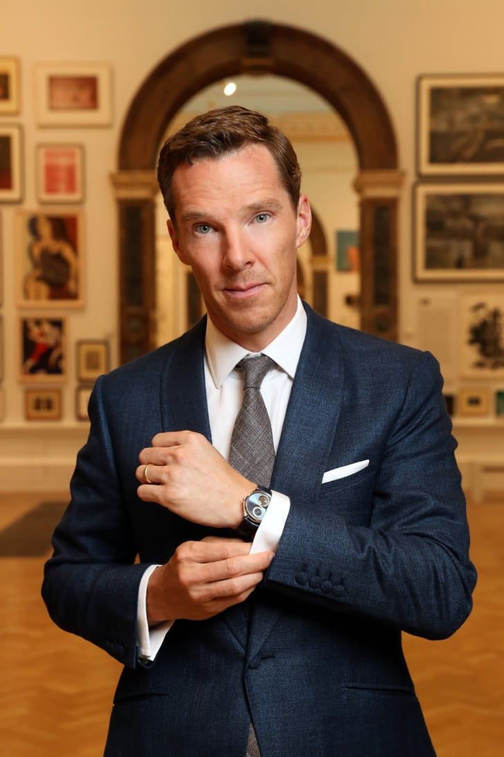 a man in a suit and tie is standing with his hands on his lapel