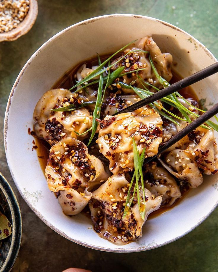 someone holding chopsticks in a white bowl filled with meat and vegetables on a table