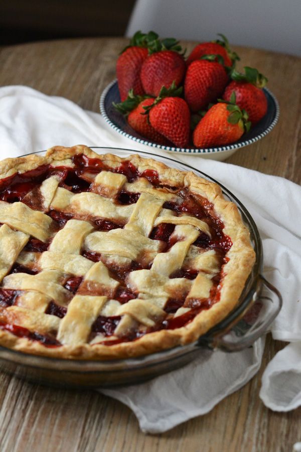 a pie sitting on top of a wooden table next to two bowls of strawberries