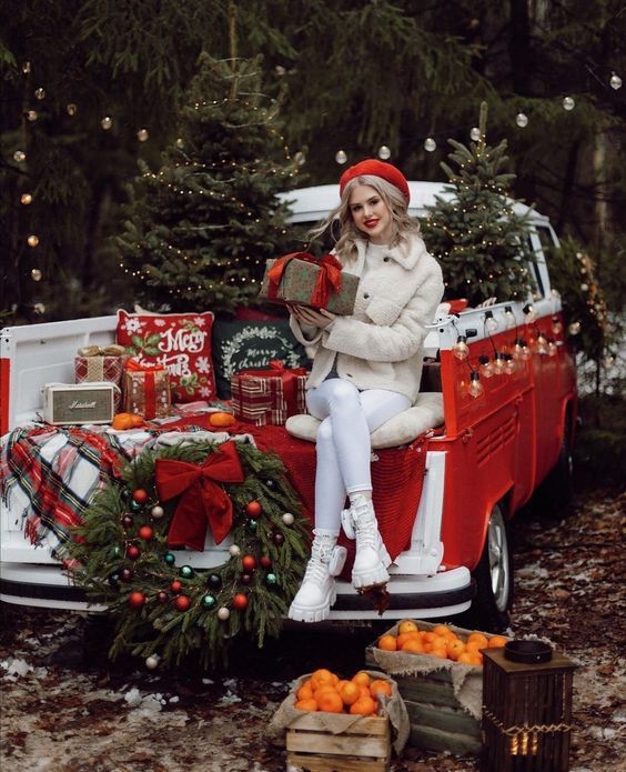 a woman sitting on the back of a red truck with christmas decorations and presents in it