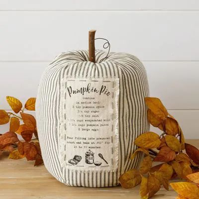 a striped pumpkin pillow sitting on top of a wooden table next to some autumn leaves